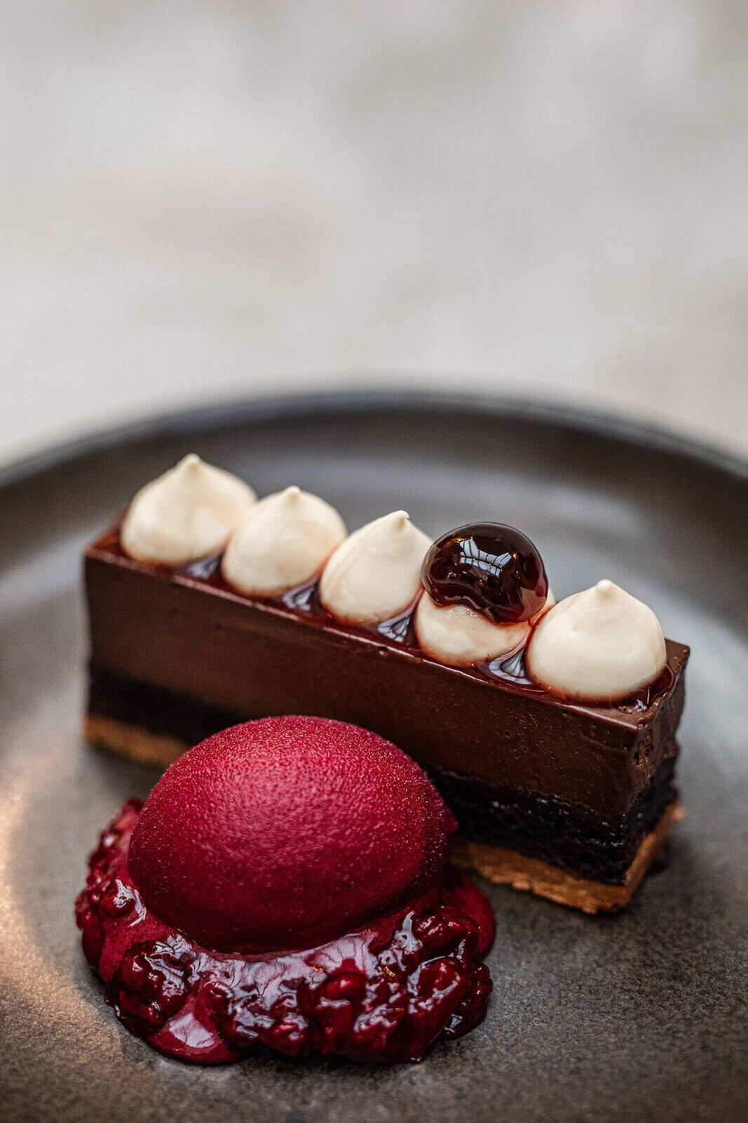 A dessert with a chocolate base, topped with white meringue and a glossy red sauce.