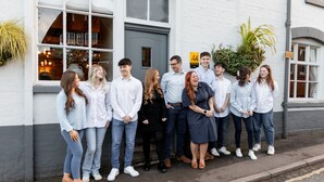 A group of people standing outside a building with a white facade and a grey door. - The Boot at Repton (Derby)