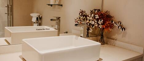 A bathroom with a large white bathtub, a sink, and a mirror. There is a shelf with toiletries and a vase with flowers on the counter.