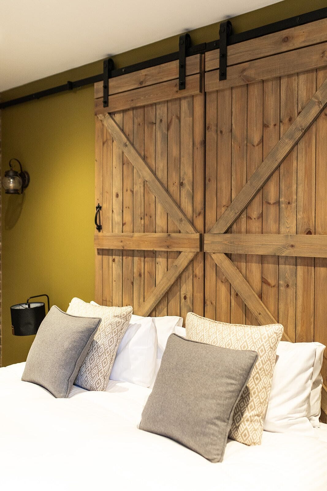 Une chambre à coucher avec une tête de lit en bois de style grange, un lit avec de nombreux oreillers et une lampe fixée au mur.