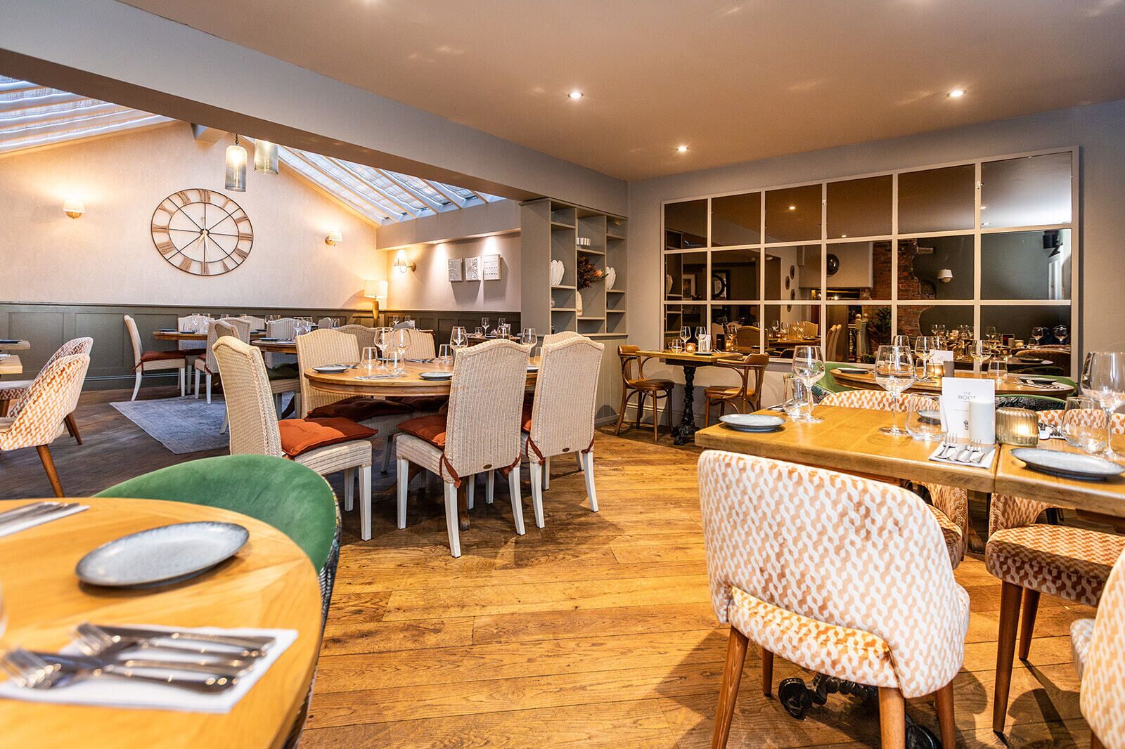 A spacious dining area with multiple tables and chairs, a large clock on the wall, and a skylight above.
