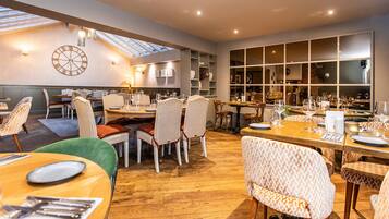 A spacious dining area with multiple tables and chairs, a large clock on the wall, and a skylight above.