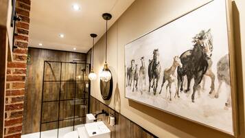 Un baño moderno con un cuadro grande de caballos, recinto de ducha de madera y lavamanos blanco.