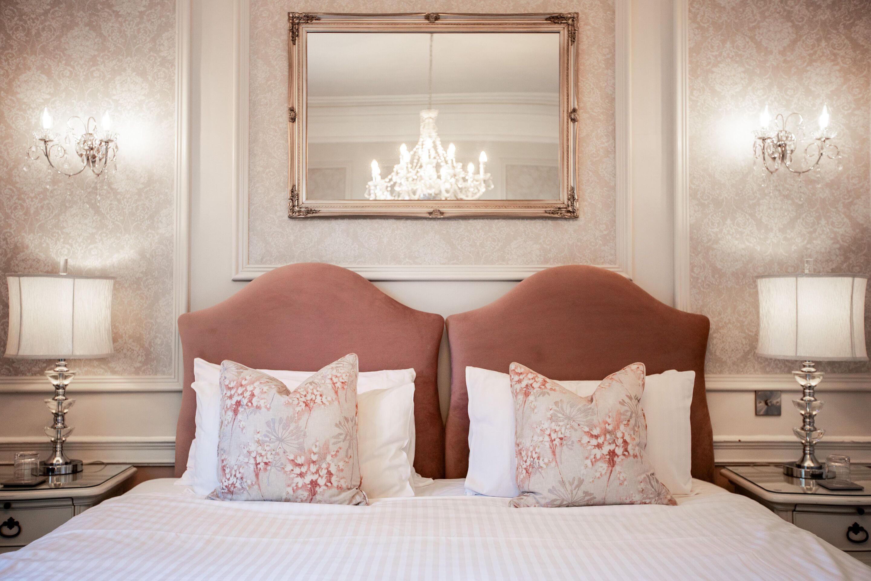 Una camera d'albergo con un letto grande, due comodini, un lampadario e uno specchio appeso al muro.