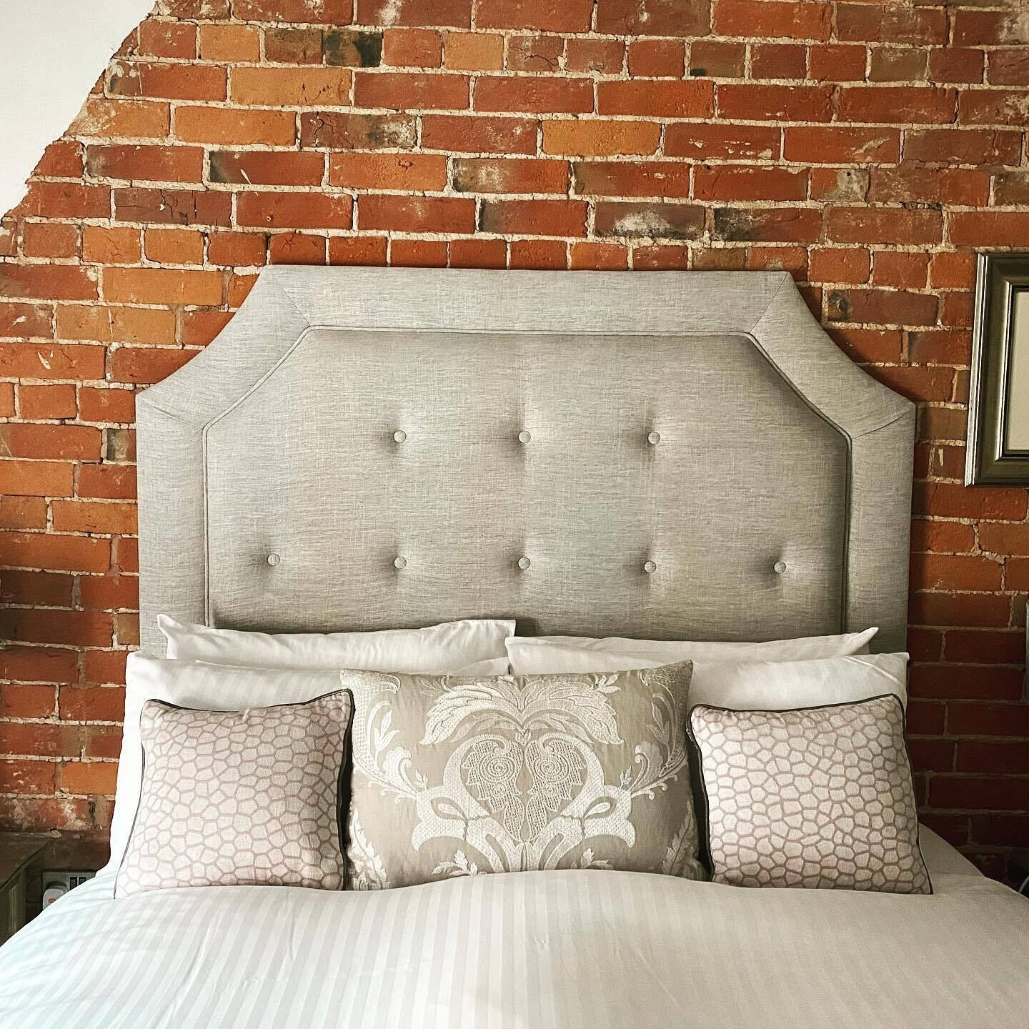 A bed with a tufted headboard against a brick wall.