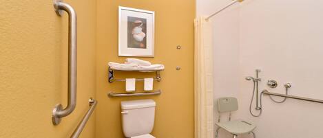 Un baño con inodoro, barras de apoyo, asiento de ducha y un perchero para toallas.