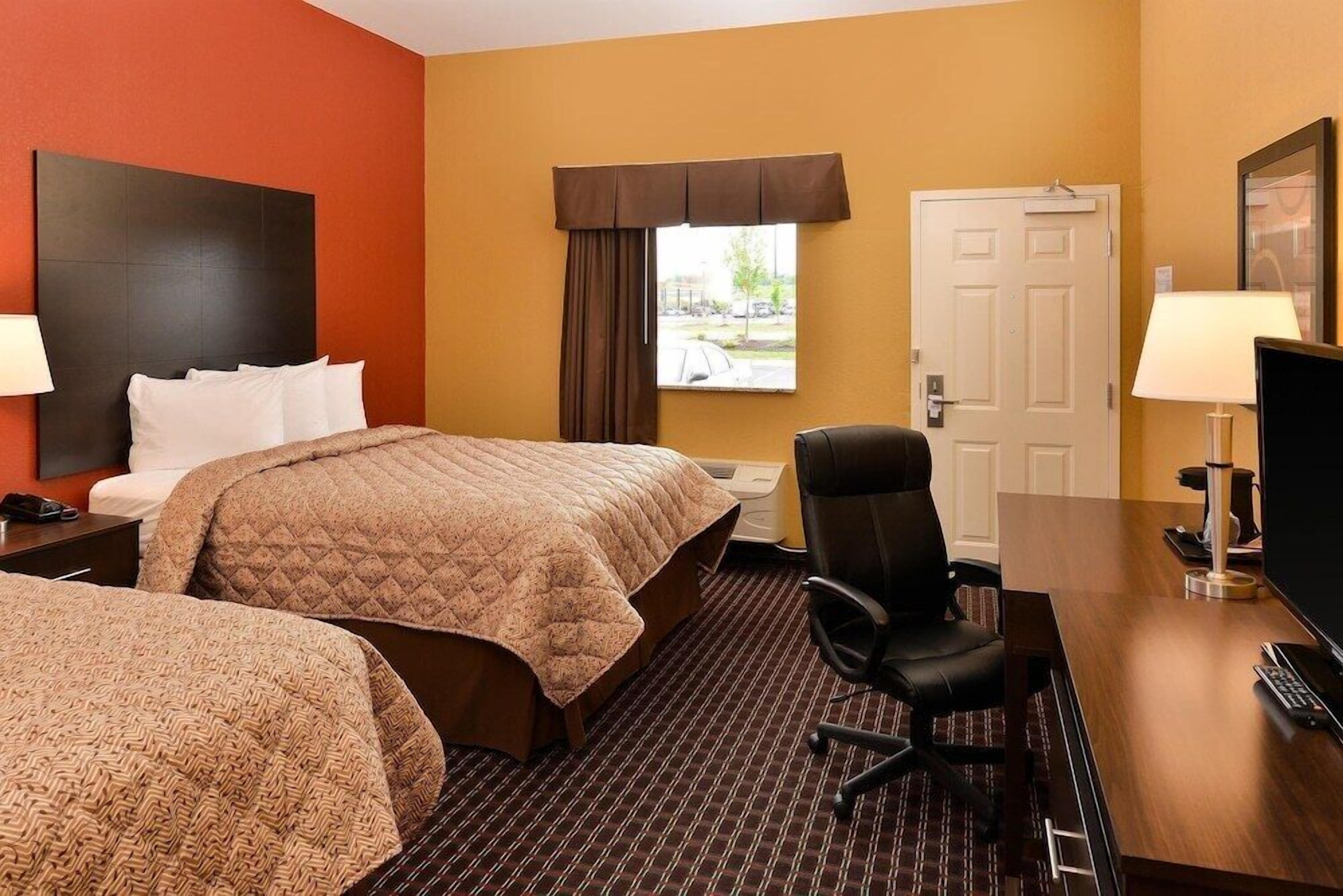 A hotel room with two beds, a desk, a chair, a television, and a window with a view of the outdoors.