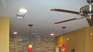 Un espace d’accueil avec un mur en pierre, un ventilateur de plafond et deux lampes suspendues.