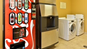 Un distributeur de boissons en libre-service proposant un choix varié, un distributeur d’eau et un espace buanderie à la disposition des clients, équipé de machines à laver.