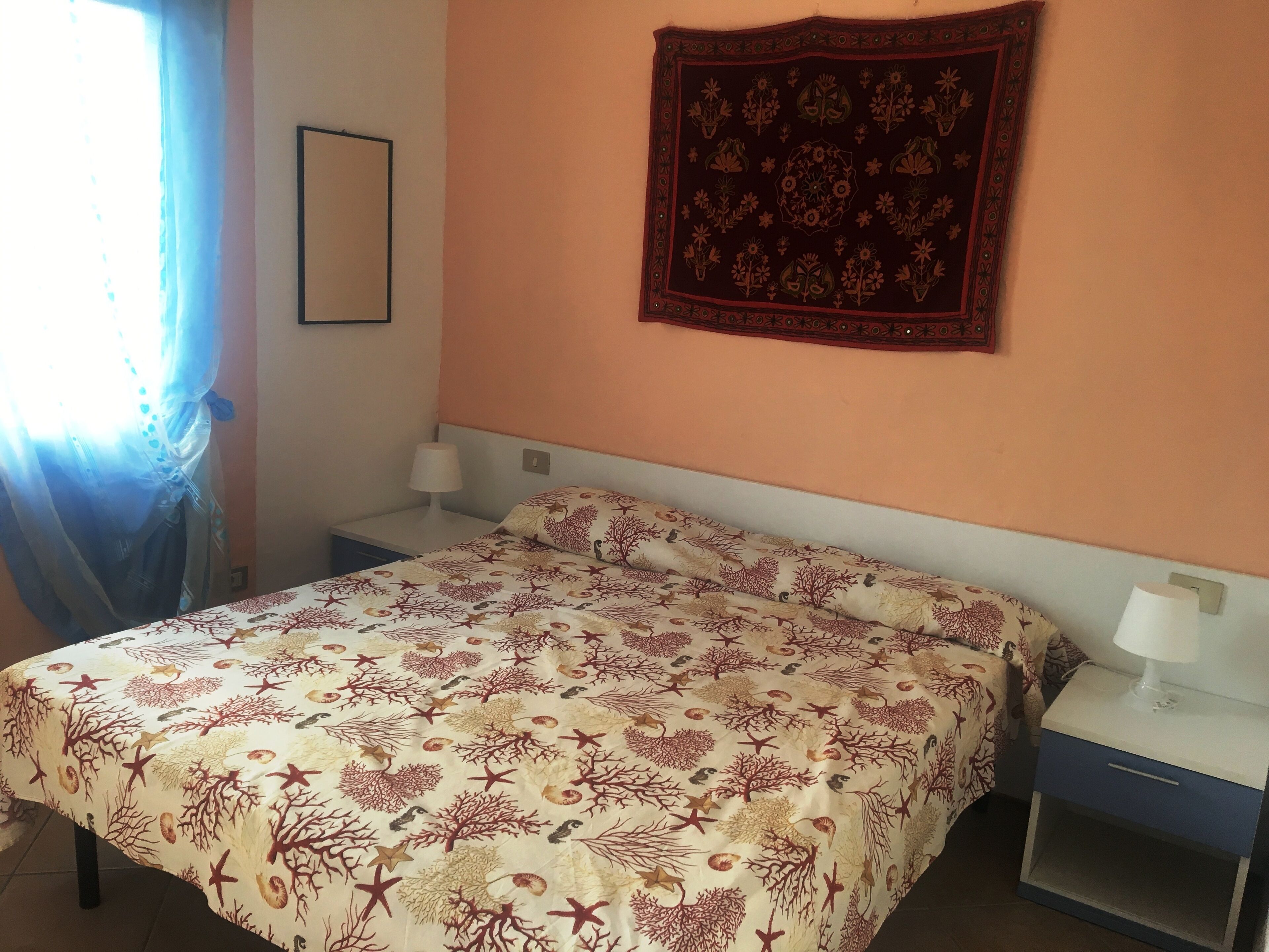 Une chambre à coucher comprenant un lit, deux tables de chevet, une commode, une tapisserie murale et une fenêtre avec des rideaux.