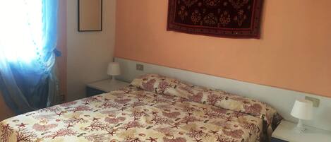 Une chambre à coucher comprenant un lit, deux tables de chevet, une commode, une tapisserie murale et une fenêtre avec des rideaux.