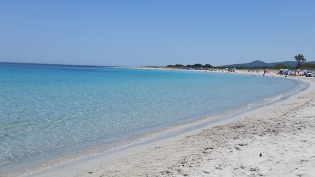 A beach with clear turquoise water, white sand, and a few people in the distance.