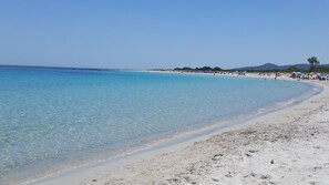 A beach with clear turquoise water, white sand, and a few people in the distance. - Porto Ottiolu Resort (Budoni)