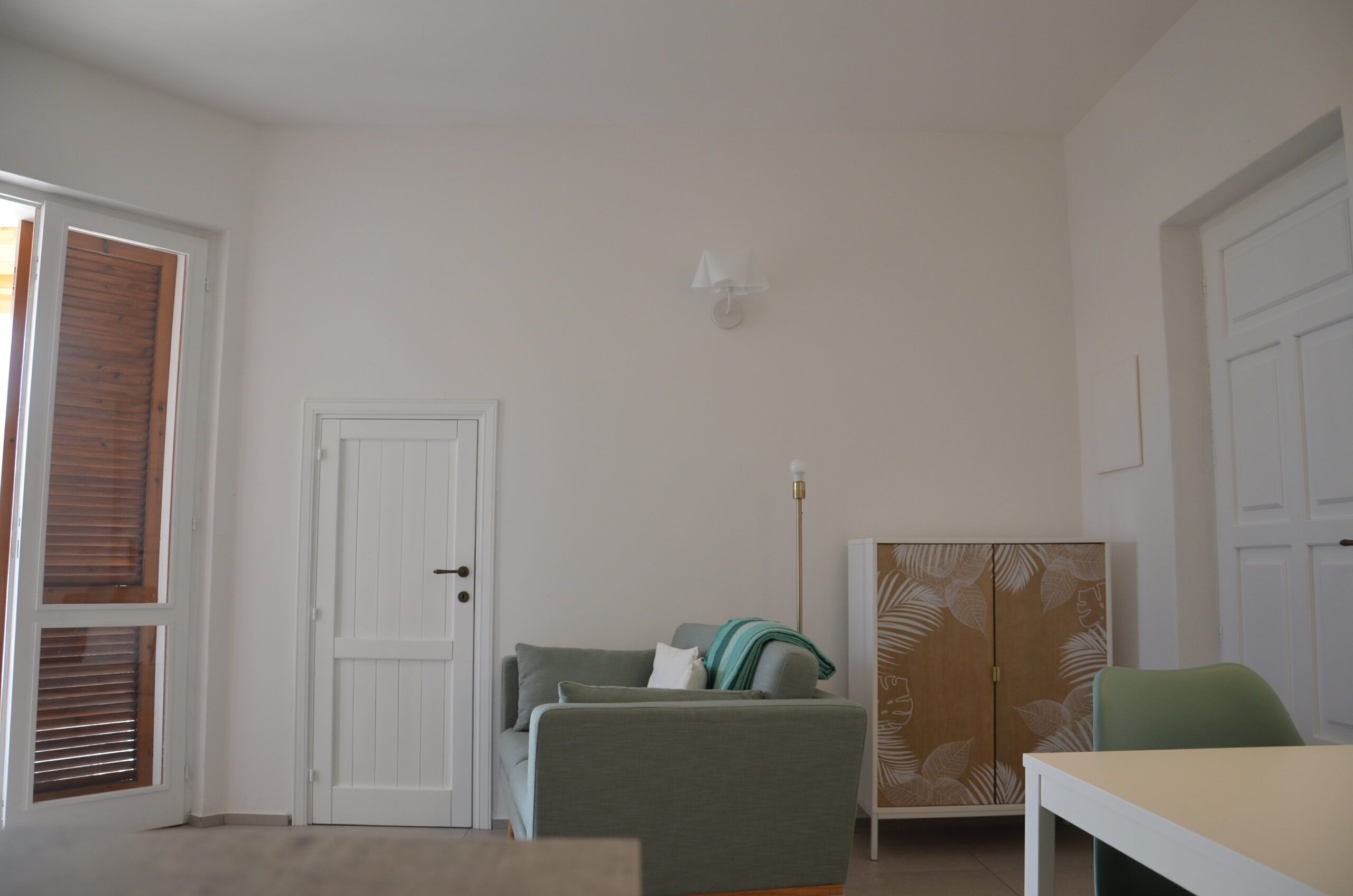 Une pièce avec une porte blanche, un canapé vert, une table et une armoire ornée de motifs végétaux.