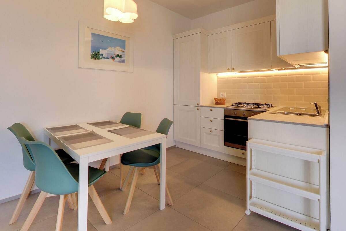 Una cocina moderna con armarios blancos, una estufa a gas y un comedor con mesa y sillas.