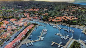 An aerial view of a coastal town with a marina filled with boats, surrounded by terraced houses with red roofs.
