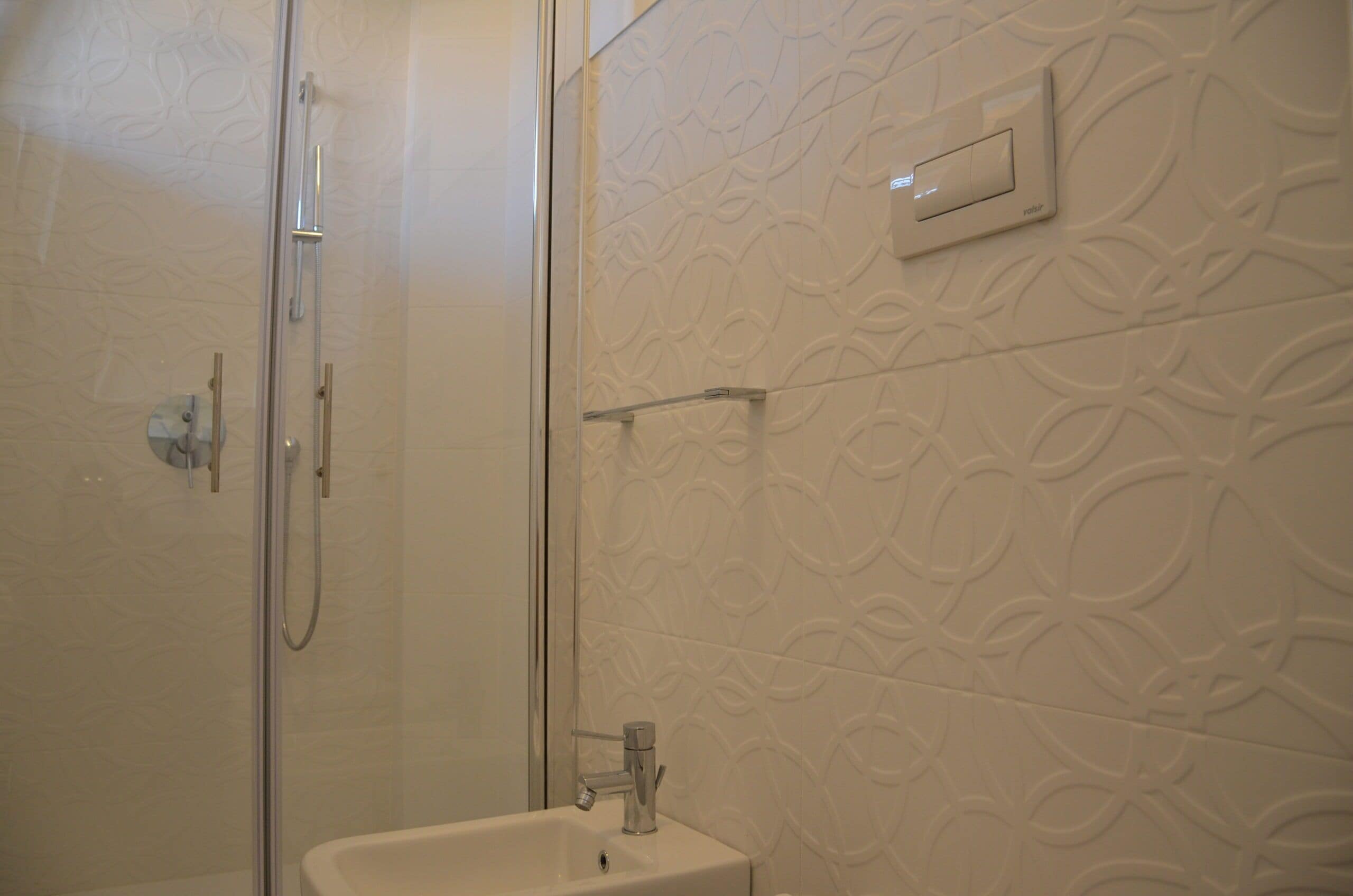 A bathroom with a glass-enclosed shower, a sink, and a wall-mounted light switch.