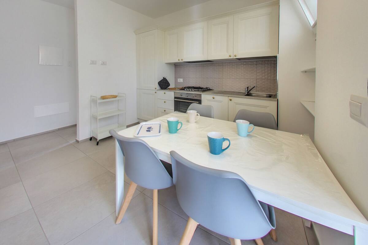 Una cocina moderna con armarios blancos, una estufa a gas y un comedor con mesa y sillas.