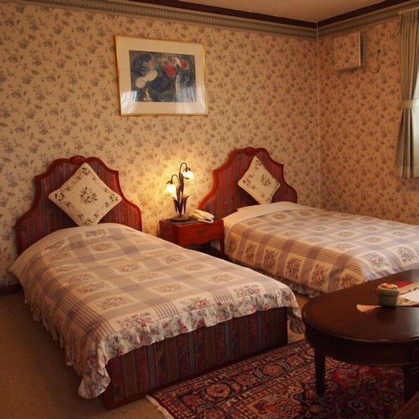 Una habitación con dos camas, una mesita de noche con lámpara, un cuadro enmarcado en la pared y una alfombra estampada.