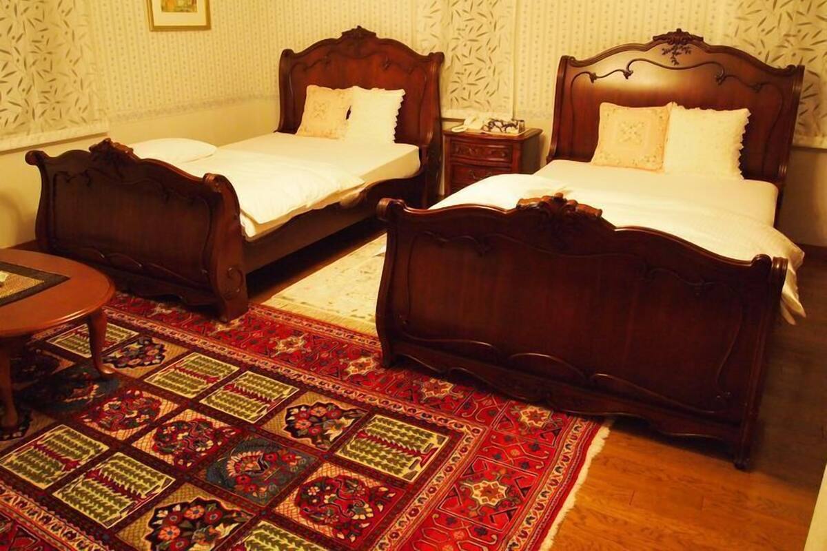 Une chambre d’hôtel avec deux lits en bois, une petite table et un tapis à motifs.