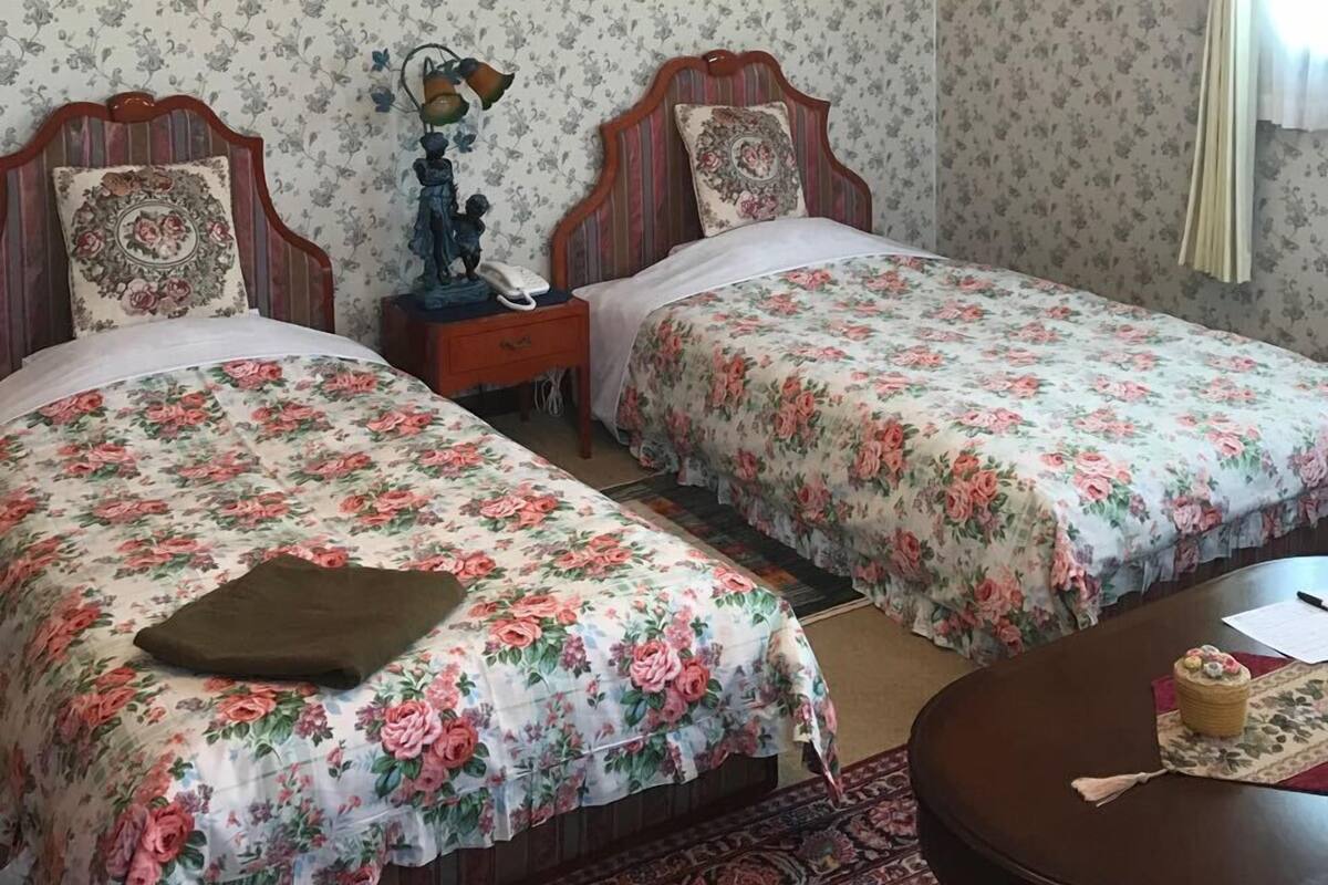 Une chambre avec deux lits, une table de chevet, un tableau encadré, un lustre et une petite table sur laquelle se trouve un panier.