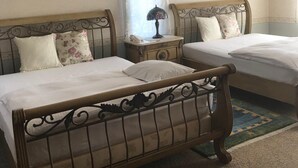 Two twin beds with ornate metal headboards, a small bedside table with a lamp, and a window with floral curtains.