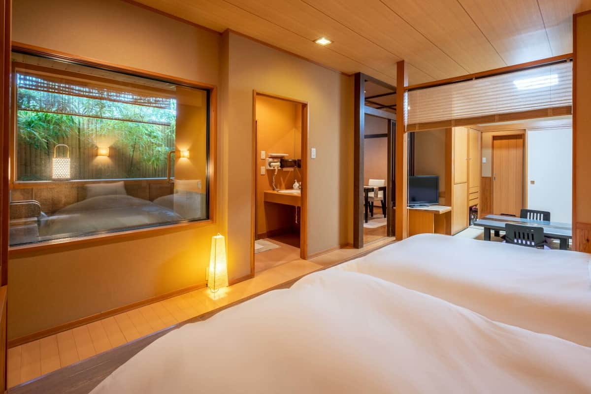 A hotel room with a large bed, a desk with a chair, a TV, and a bathroom with a sink and mirror.