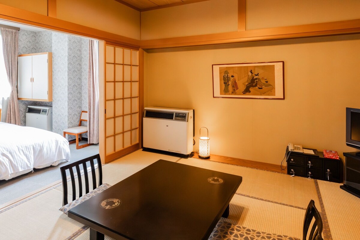 A hotel room with a bed, a desk, a chair, a TV, a heater, and a picture on the wall.