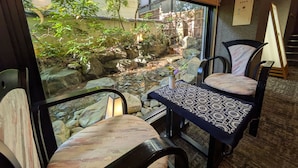 A dining area with a view of a garden, a table with a patterned tablecloth, and chairs with cushions. - Ryokan Hiromitei (Hanamaki)