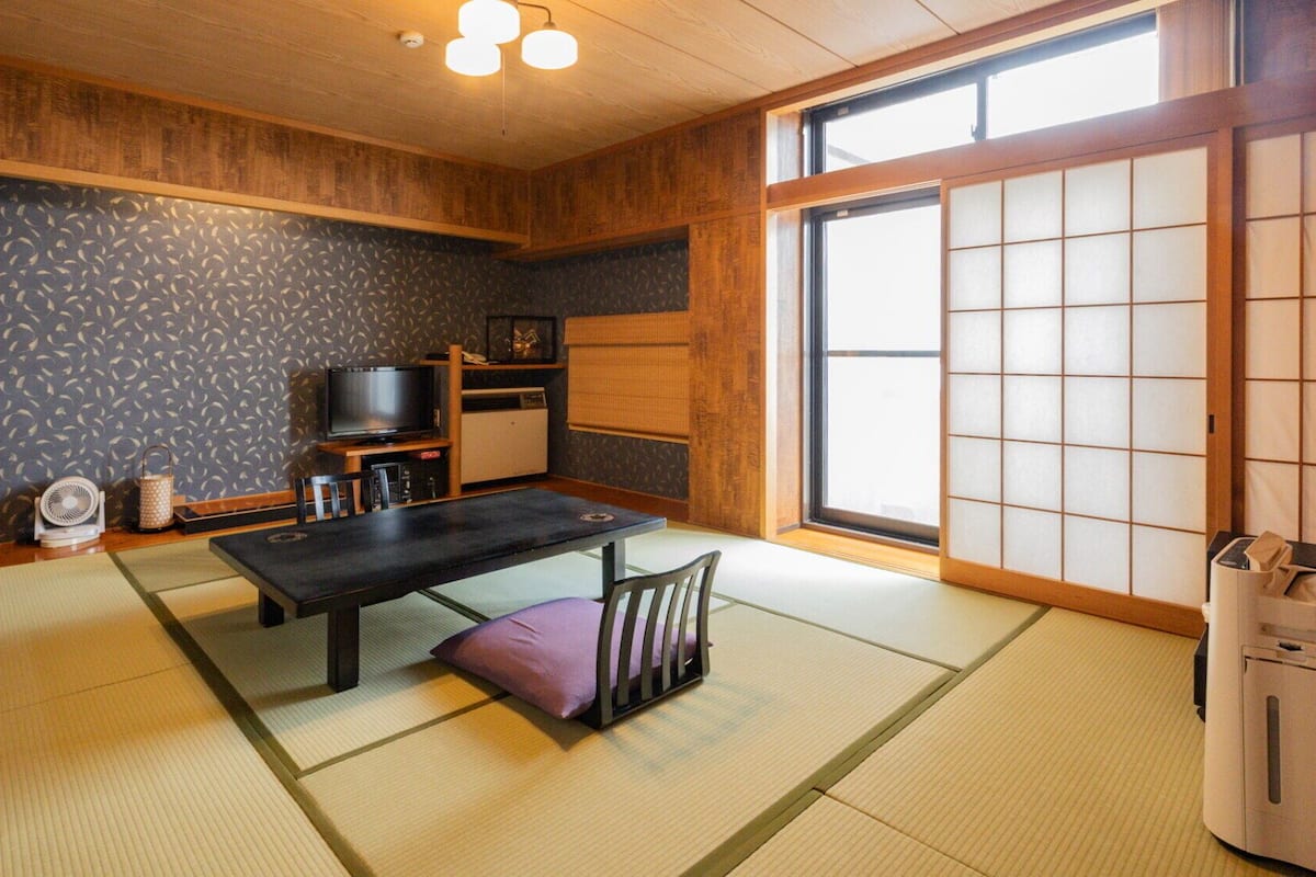 A traditional Japanese room with tatami flooring, a low table, a television, and a sliding door.