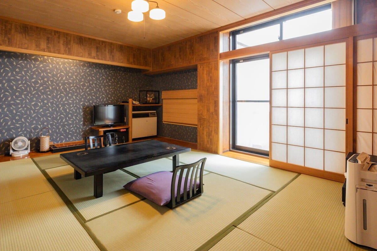 A traditional Japanese room with tatami flooring, a low table, a television, and a sliding door.