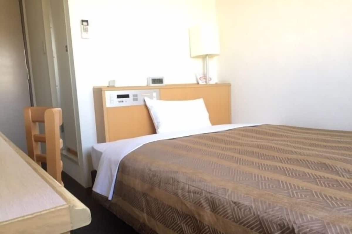 Une chambre d’hôtel avec un lit simple, une tête de lit en bois, une table de chevet et une lampe.