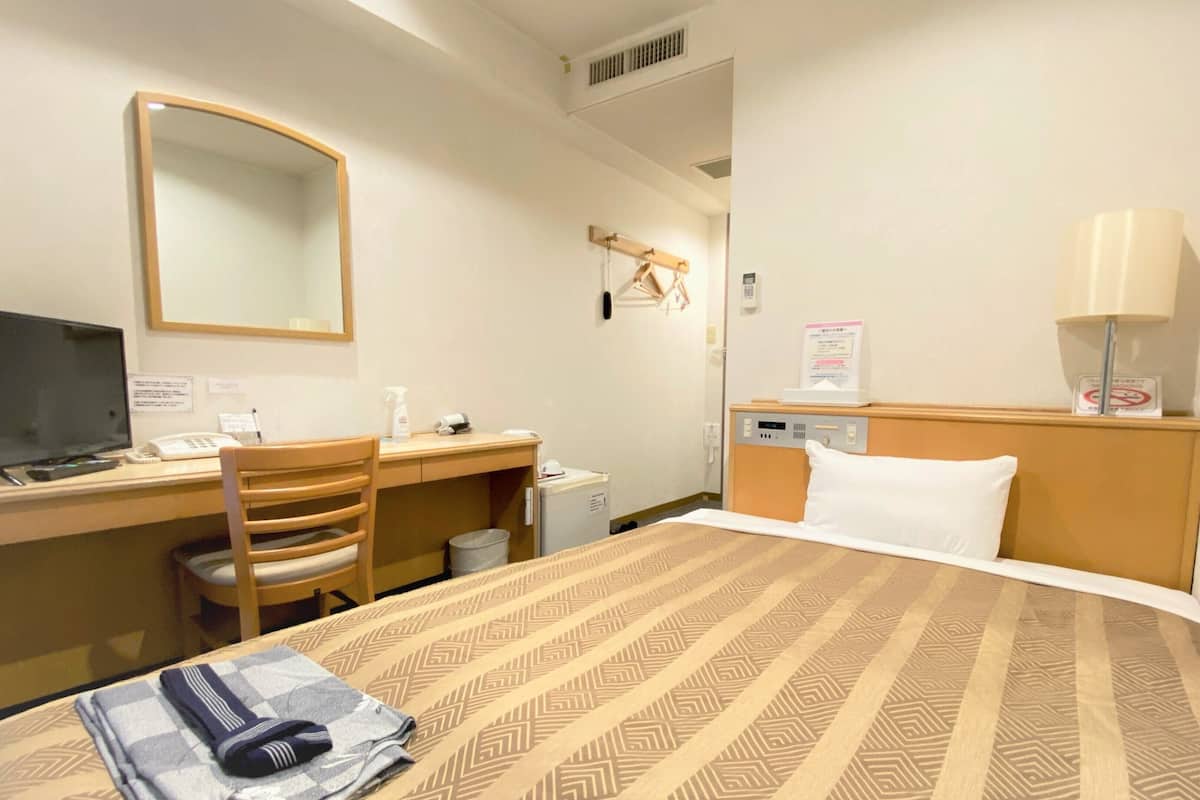 Une chambre d’hôtel équipée d’un lit, d’un bureau, d’une chaise, d’une télévision et d’un miroir.