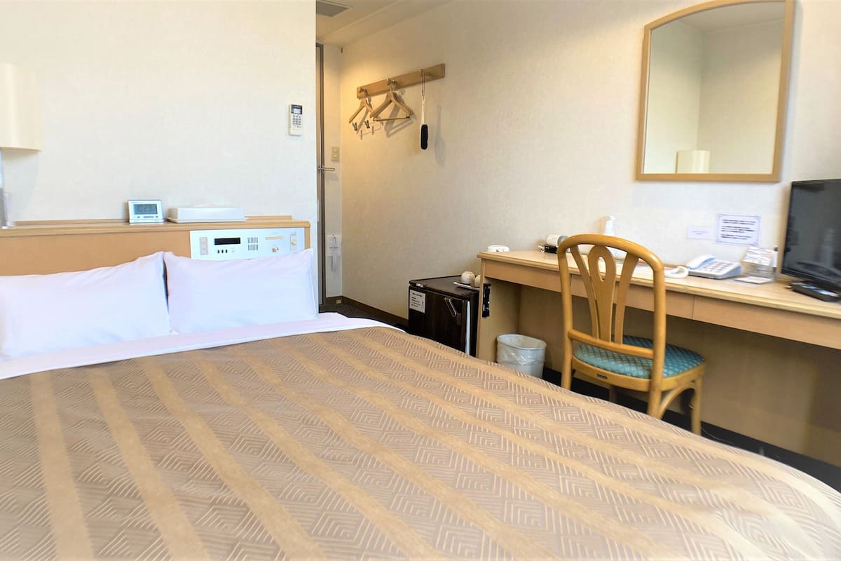 Une chambre d’hôtel équipée d’un lit, d’un bureau avec un ordinateur et un téléphone, d’une chaise et d’un téléviseur.