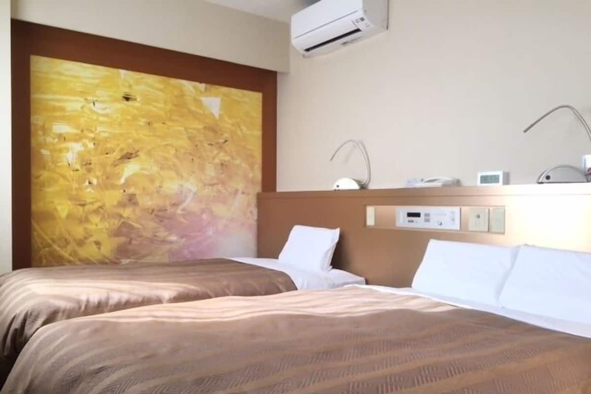 Une chambre d’hôtel avec deux lits, une grande peinture abstraite au mur, un appareil de climatisation et un panneau de commande.