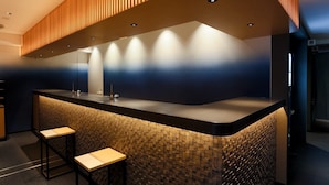 A modern bar area with a curved counter, two stools, and a patterned wall. - Hotel New Shohei (Tokyo)
