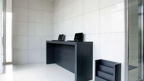 A reception desk with a dark finish, white tiled walls, and a glass partition.