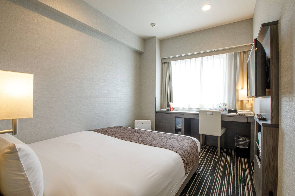 A hotel room with a large bed, a desk with a chair, a television, and a window with curtains.