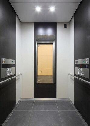 An elevator with a control panel on each side, a door with a light panel, and a tiled floor.
