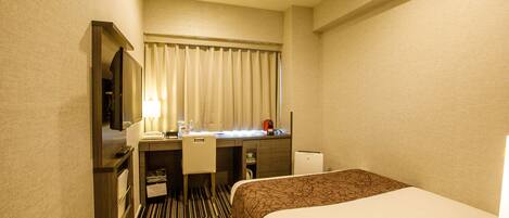 A hotel room with a bed, a desk with a chair, a television, and a window with curtains.