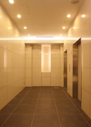 A corridor with tiled walls and floor, a central light fixture, and an elevator on the right. - Hotel Sunroute Fukuchiyama (Fukuchiyama)