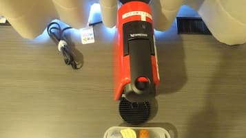 Une machine à café Nespresso rouge, avec un compartiment pour les capsules de café et un câble d’alimentation, posée sur une surface en bois.