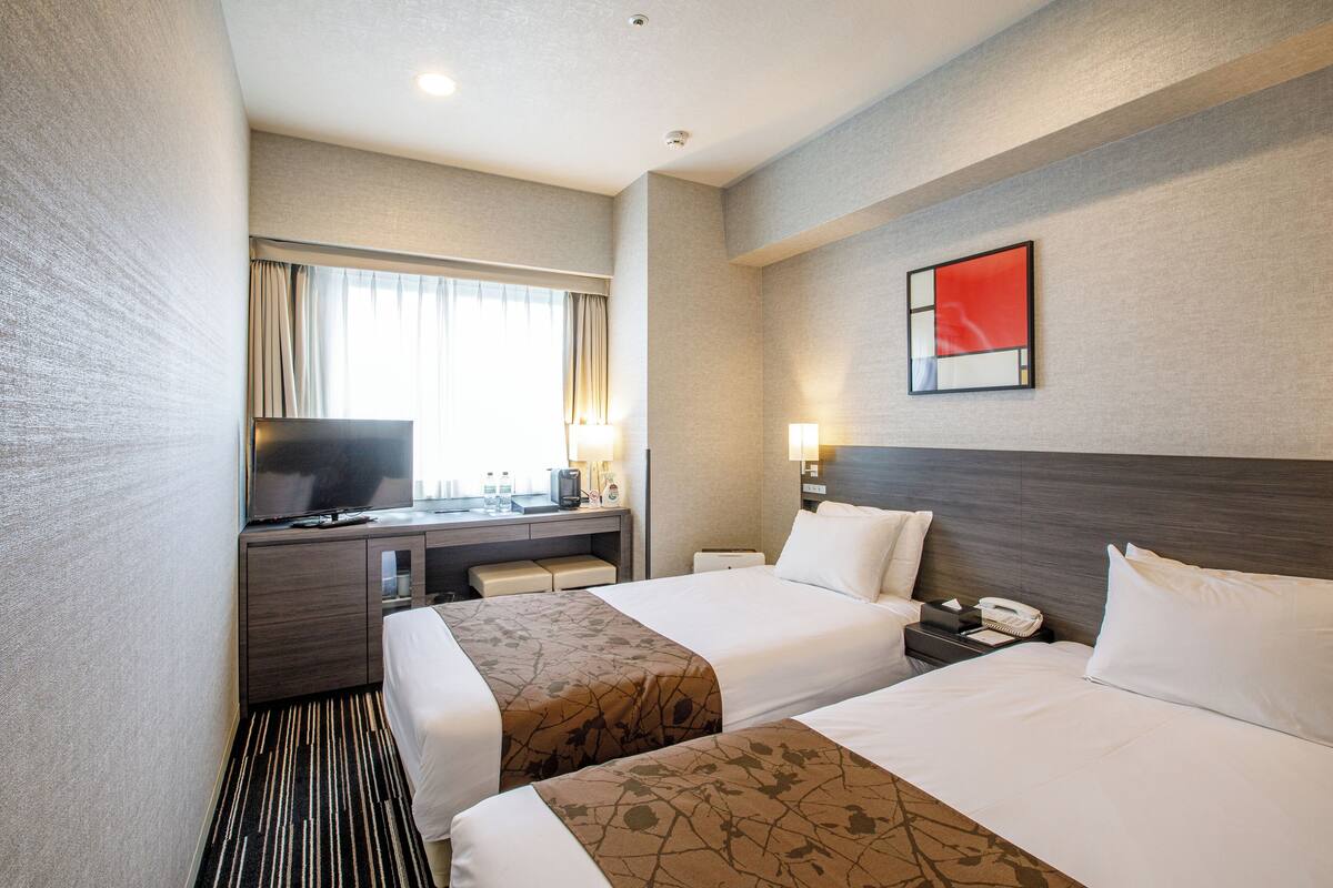 A hotel room with two beds, a desk with a television, a window with curtains, and a painting on the wall.