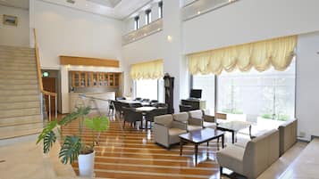 A spacious living area with a wooden floor, a dining set, sofas, and a television.