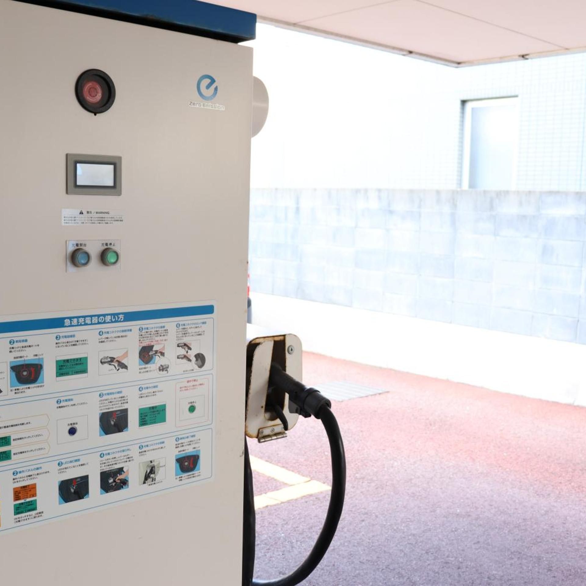 Une borne de recharge publique, dotée d’un panneau de commande, d’un panneau d’avertissement de sécurité et d’un mur en arrière-plan.