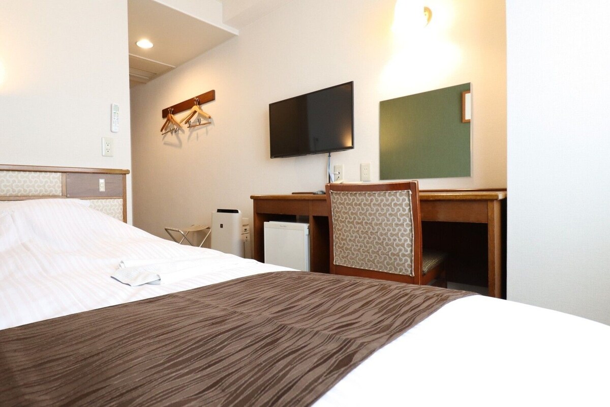 A hotel room with a bed, a desk, a chair, a television, and a mirror.