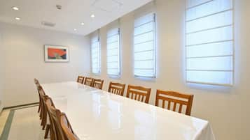 A conference room with a long table and wooden chairs, large windows, and a framed picture on the wall.