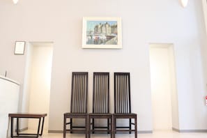 Una habitación con tres sillas de madera oscura, una mesa blanca y un cuadro en la pared.