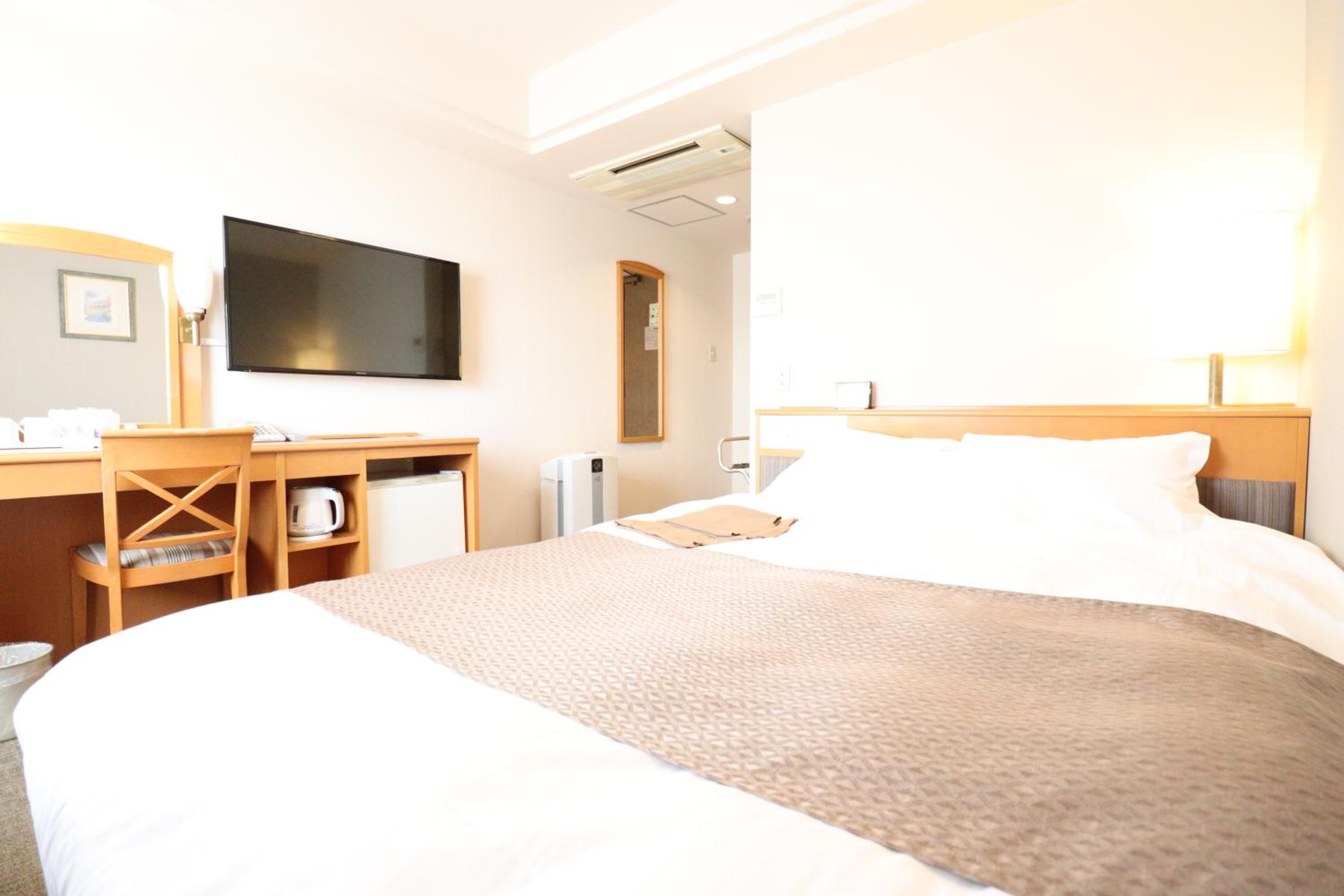 A hotel room with a bed, a desk, a television, and an air conditioning unit.