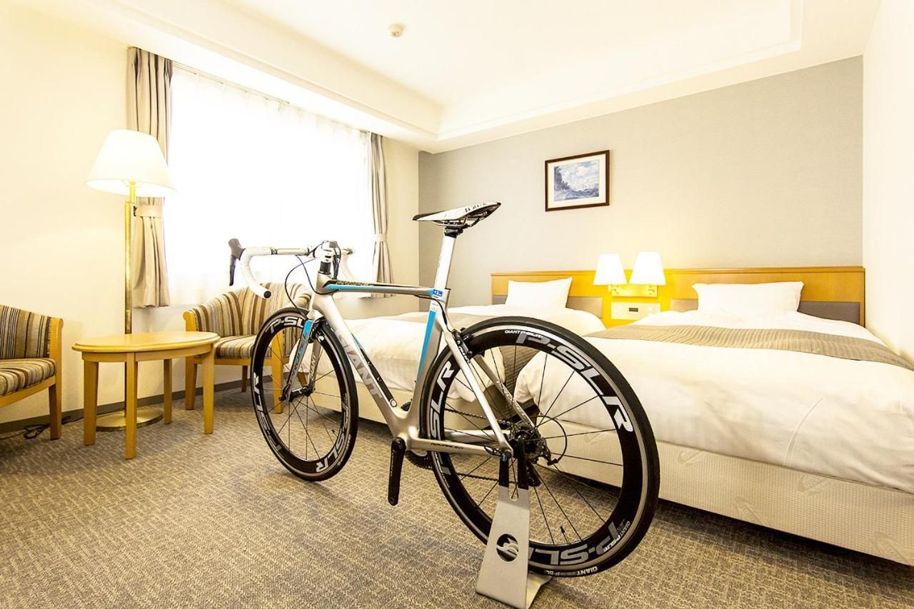 A hotel room with a bed, a sofa, a table, a lamp, and a bicycle.